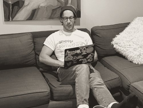Michael Makarov on a couch, typing on a laptop covered in stickers